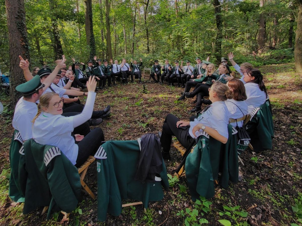 Mitglieder des Spielmannszug Rhede bei einem Gruppenausflug im Wald, alle lächeln herzlich in die Kamera und zeigen den Zusammenhalt der Gemeinschaft
